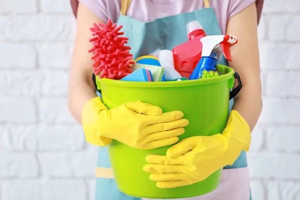 Woman holding bucket with cleaning supplies on brick wall background — Stock Photo, Image