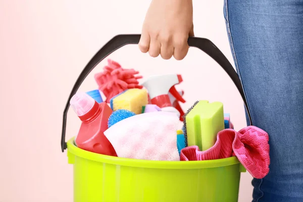 Frau hält Eimer mit Putzmitteln auf farbigem Hintergrund — Stockfoto