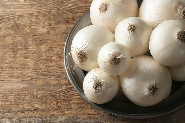 Plate with ripe onions on wooden table — Stock Photo, Image