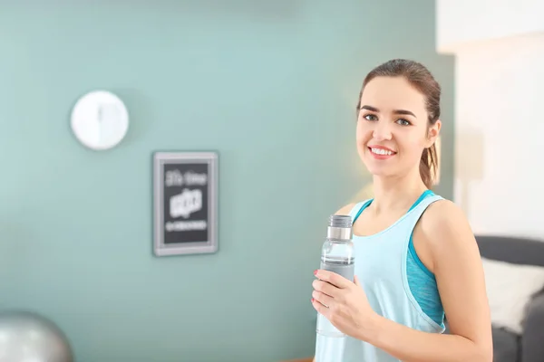 Mulher bonita com garrafa de água depois de fazer exercícios de fitness em casa — Fotografia de Stock