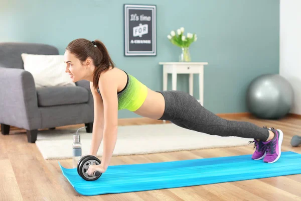 Beautiful young woman doing fitness exercise with roller wheel at home — Stock Photo, Image