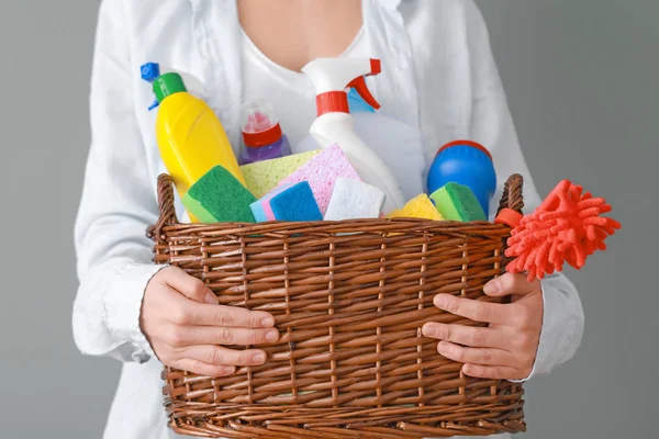 Woman holding basket with cleaning supplies on grey background — Stock Photo, Image