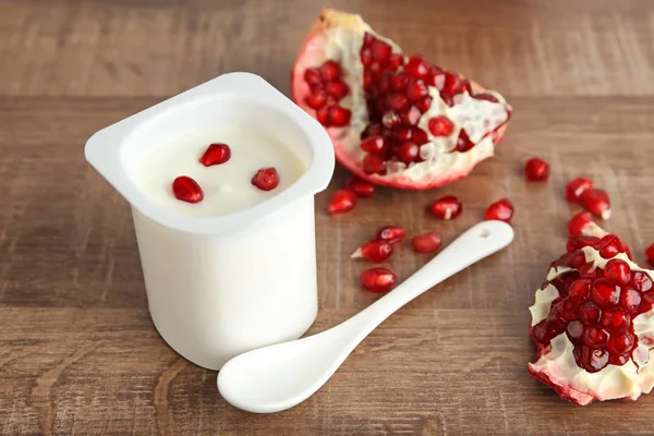 Bicchiere di plastica di yogurt gustoso con semi di melograno sul tavolo di legno — Foto Stock