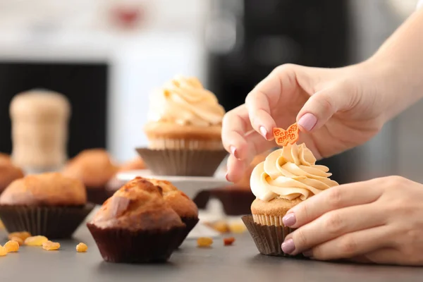 Vrouw versieren van lekkere cupcake aan tafel — Stockfoto