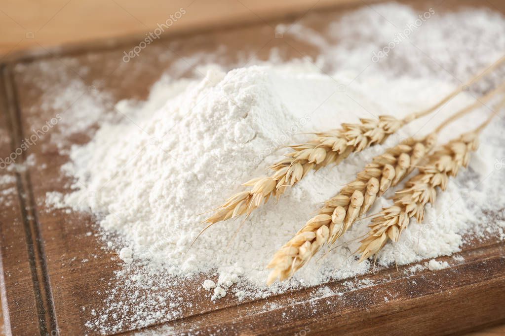 Wheat flour and spikes on wooden board, closeup