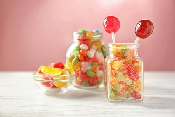 Gläser mit verschiedenen Bonbons und Succades auf dem Tisch vor farbigem Hintergrund — Stockfoto