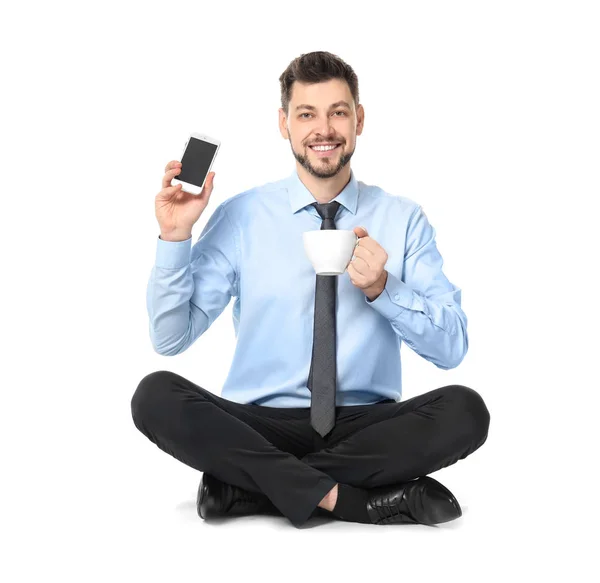 Молодой бизнесмен с телефоном и чашкой кофе сидит в позе лотоса на белом фоне — стоковое фото
