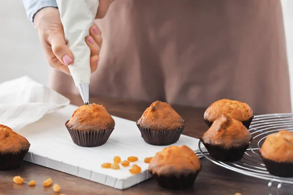 Mujer decorando sabrosos cupcakes con crema en la mesa — Foto de Stock