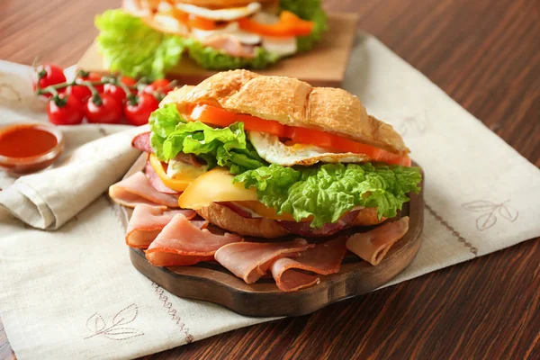 Деревянная доска с вкусным бутербродом с круассаном на столе — стоковое фото