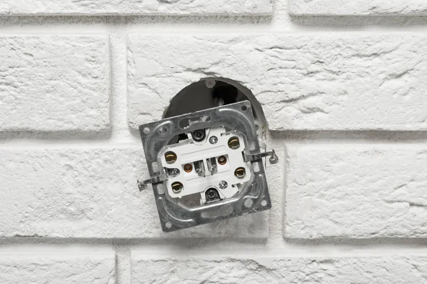 Tomada elétrica velha pendurada fora da parede de tijolo — Fotografia de Stock