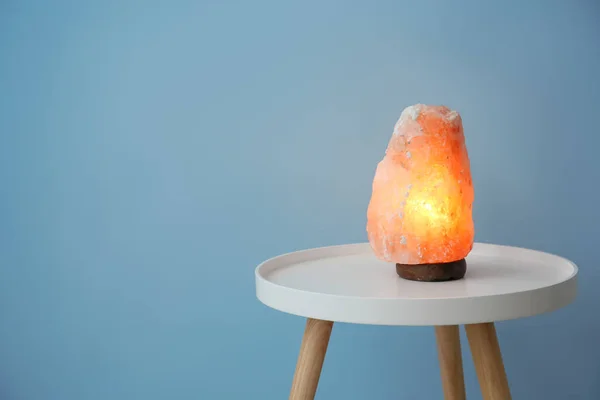 Himalayan salt lamp on table against color background