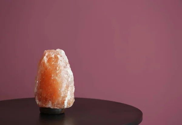 Himalayan salt lamp on table against color background — Stock Photo, Image