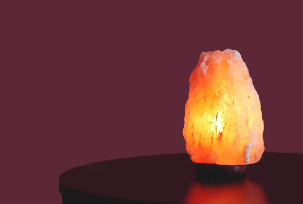 Himalayan salt lamp on table against color background — Stock Photo, Image