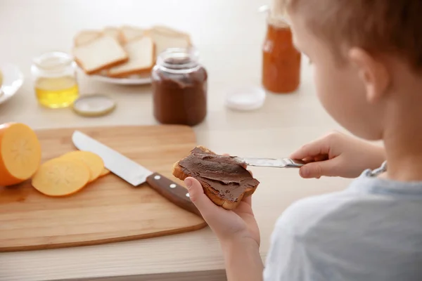 Liten pojke sprider choklad pasta på toast i köket — Stockfoto