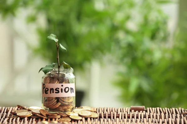 Planta que cresce a partir de frasco de vidro com moedas na superfície de vime contra fundo desfocado. Conceito de planeamento de pensões — Fotografia de Stock