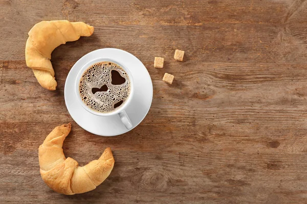 Gustosi rotoli di mezzaluna e una tazza di caffè su sfondo di legno — Foto Stock