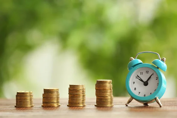 Composition with stacks of coins and alarm clock on blurred background. Time for pension planning — Stock Photo, Image