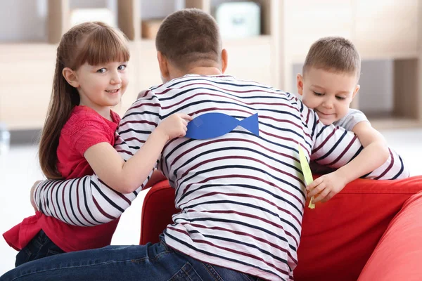 Los niños pequeños pegando peces de papel a la espalda de su padre en el interior. Broma del día del tonto de abril — Foto de Stock