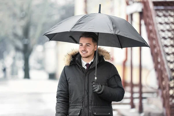 Jonge man in warme kleren met donkere paraplu buitenshuis — Stockfoto