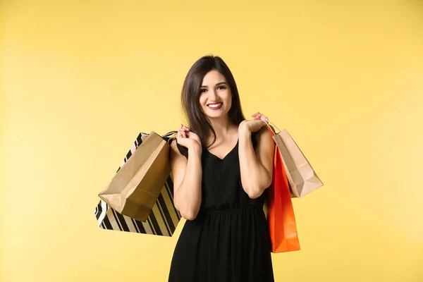 Schöne junge Frau mit Einkaufstaschen auf farbigem Hintergrund — Stockfoto