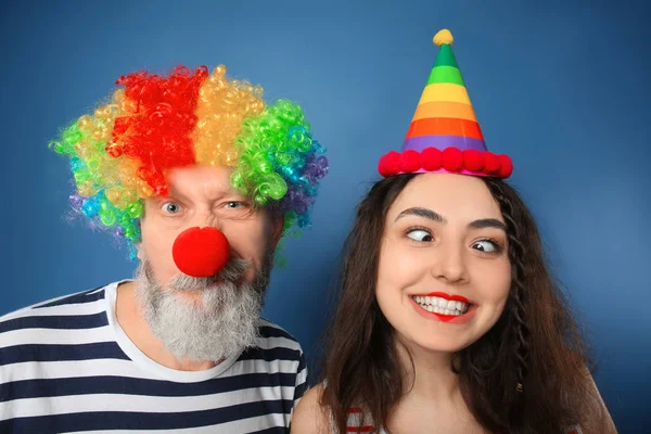 Ung kvinna och mogen man i roliga förklädnad på färgbakgrund. April fool's day firande — Stockfoto