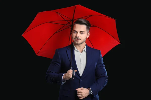 Молодой человек в элегантном костюме с красным зонтиком на черном фоне — стоковое фото