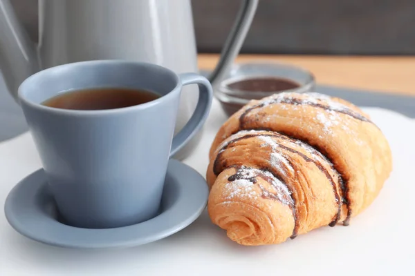 Croissant saboroso perto de xícara de café na mesa — Fotografia de Stock