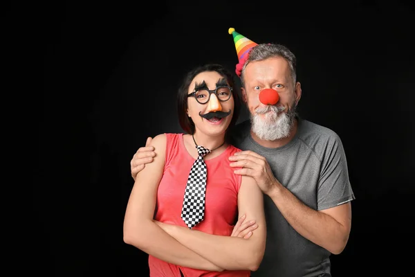 Young woman and mature man in funny disguise on dark background. April fool's day celebration — Stock Photo, Image