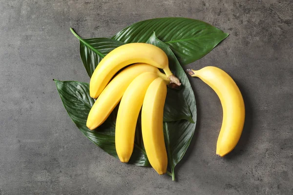 Plátanos frescos y maduros con hojas sobre fondo gris —  Fotos de Stock