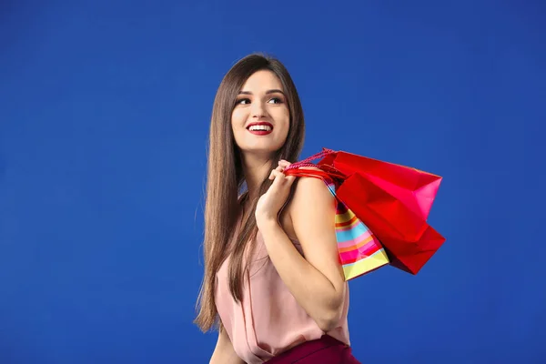 Mooie jonge vrouw met boodschappentassen op kleur achtergrond — Stockfoto