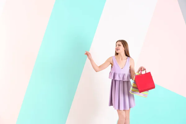 Belle jeune femme avec des sacs à provisions sur fond de couleur — Photo