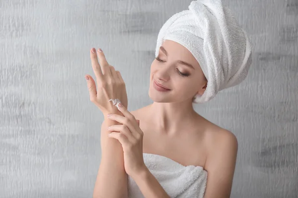 Jeune femme appliquant crème pour les mains sur fond gris — Photo