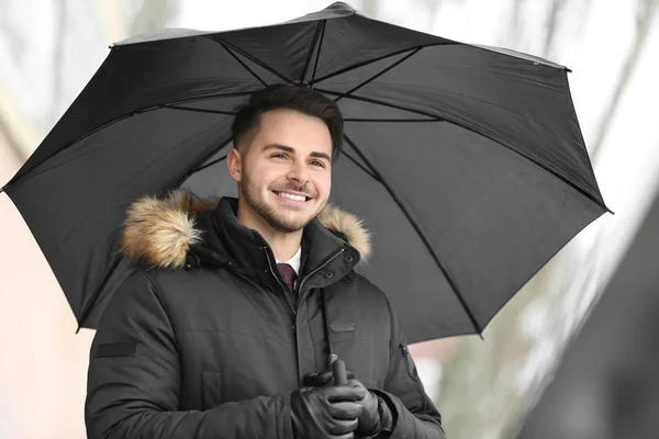 Mladý muž v teplé oblečení s tmavě deštník venku — Stock fotografie