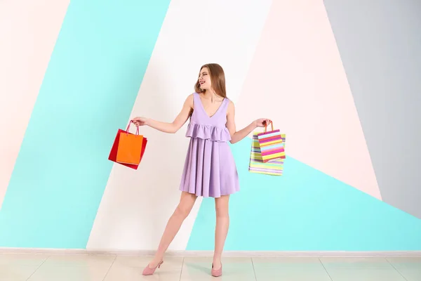 Beautiful young woman with shopping bags against color wall — Stock Photo, Image