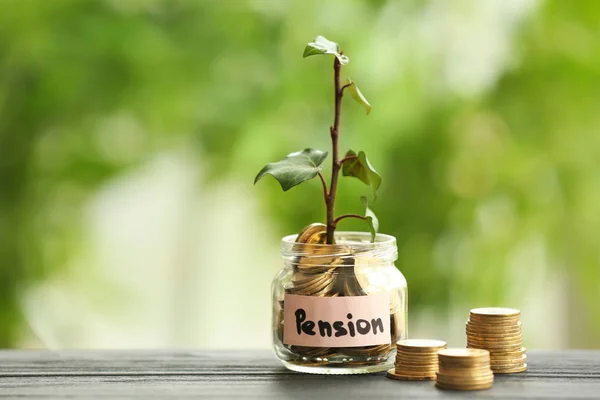 Plant growing from glass jar with coins on table against blurred background. Pension planning concept — Stock Photo, Image