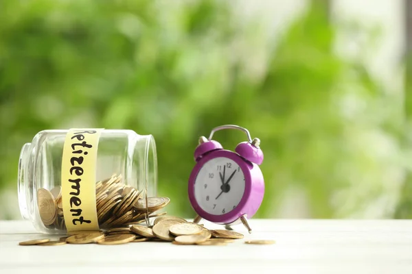 Glass jar with coins and alarm clock on blurred background. Time for pension planning — Stock Photo, Image