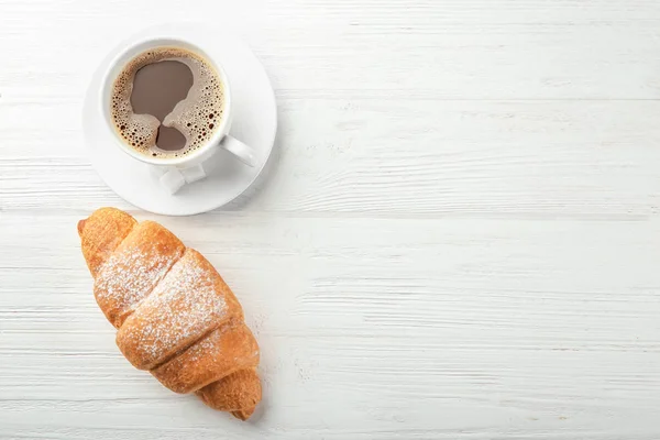 Tasty croissant and cup of coffee on wooden table — Stock Photo, Image