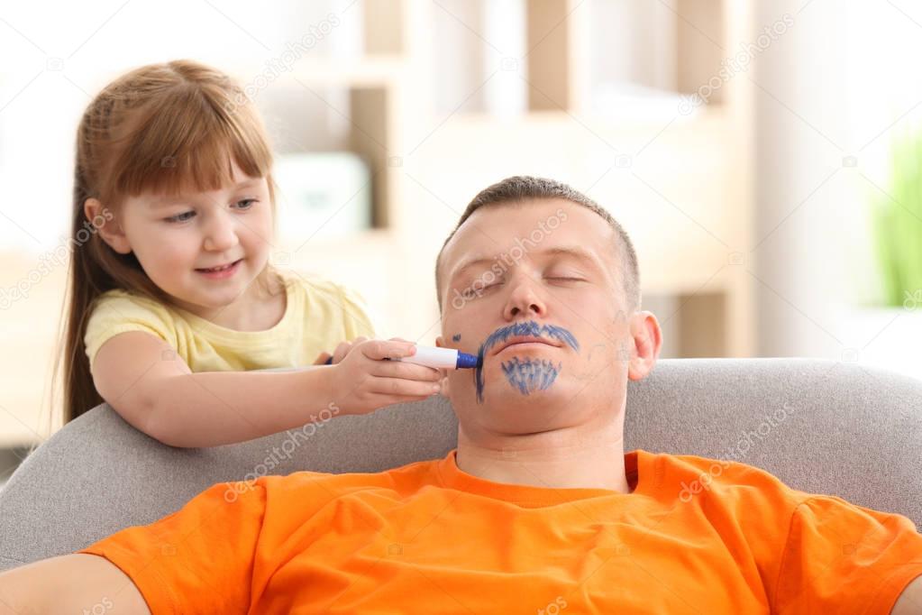 Little girl painting her father's face while he sleeping. April fool's day prank