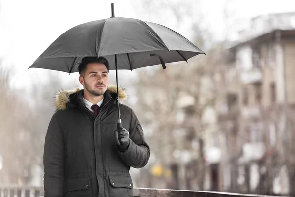 stock image Young man in warm clothes with dark umbrella outdoors