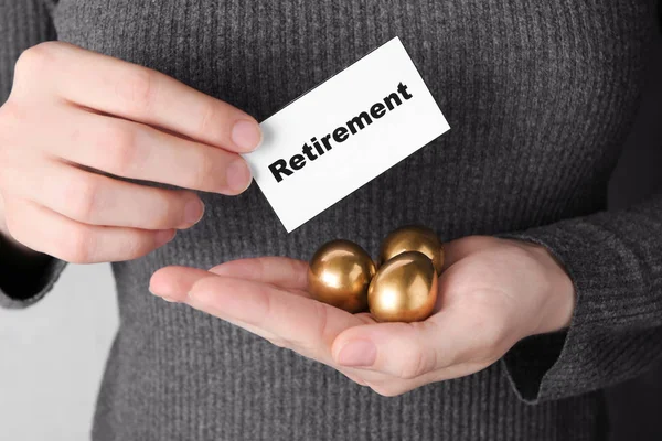 Woman holding golden eggs and sign RETIREMENT, closeup. Pension planning — Stock Photo, Image