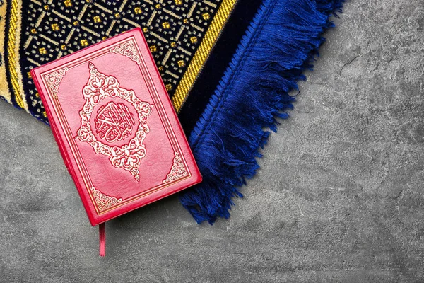 Holy book of Muslims and prayer rug on gray background