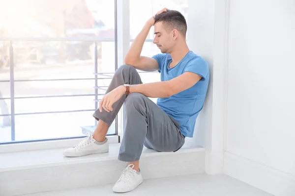 Unglücklicher junger Mann sitzt am Fenster — Stockfoto