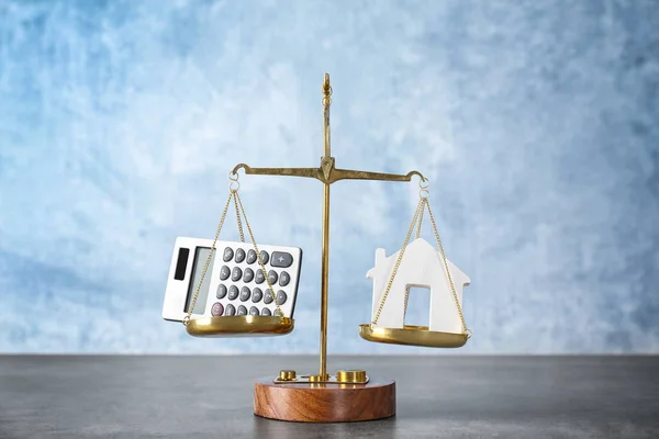Scales with calculator and house figure on table. Concept of balance between work and personal life