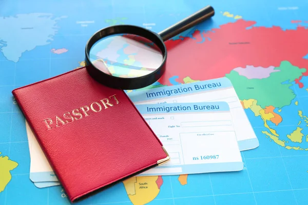 Magnifying glass and passport with arrival cards of immigration bureau on world map — Stock Photo, Image