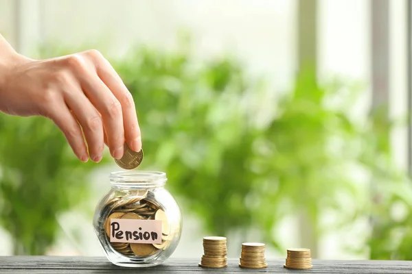 Hand legt Münze in Glas vor verschwommenem Hintergrund. Rentenplanungskonzept — Stockfoto