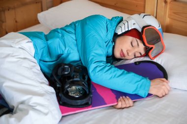 Yatakta uyuyan snowboard spor kıyafetlerle kadın. Kış tatili