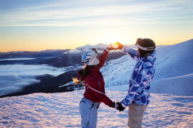 Güzel çift karlı tepe üzerinde kalp şeklinde günbatımında ellerimi. Kış tatili