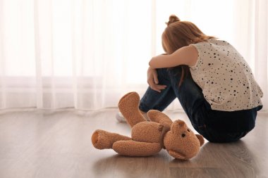 Boş oda penceresinde yakın katta oturan bir oyuncak ayı ile küçük kız. Otizm kavramı