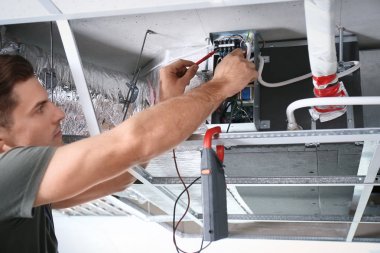 Male technician measuring voltage during repair of industrial air conditioner indoors clipart
