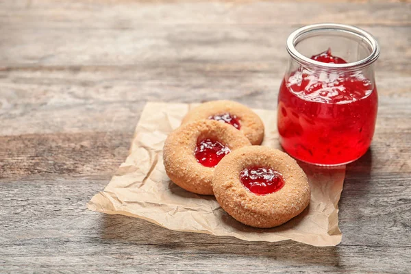 Tasty cookies with jam in jar on table